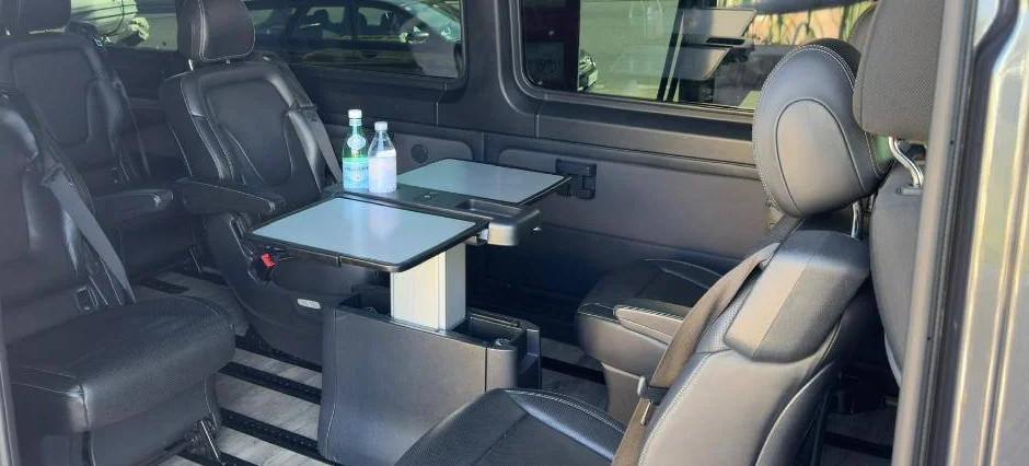Facing leather seats in the minivan cabin, tables out and water bottles set